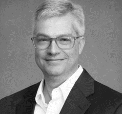 A man with glasses and white hair wearing a suit.