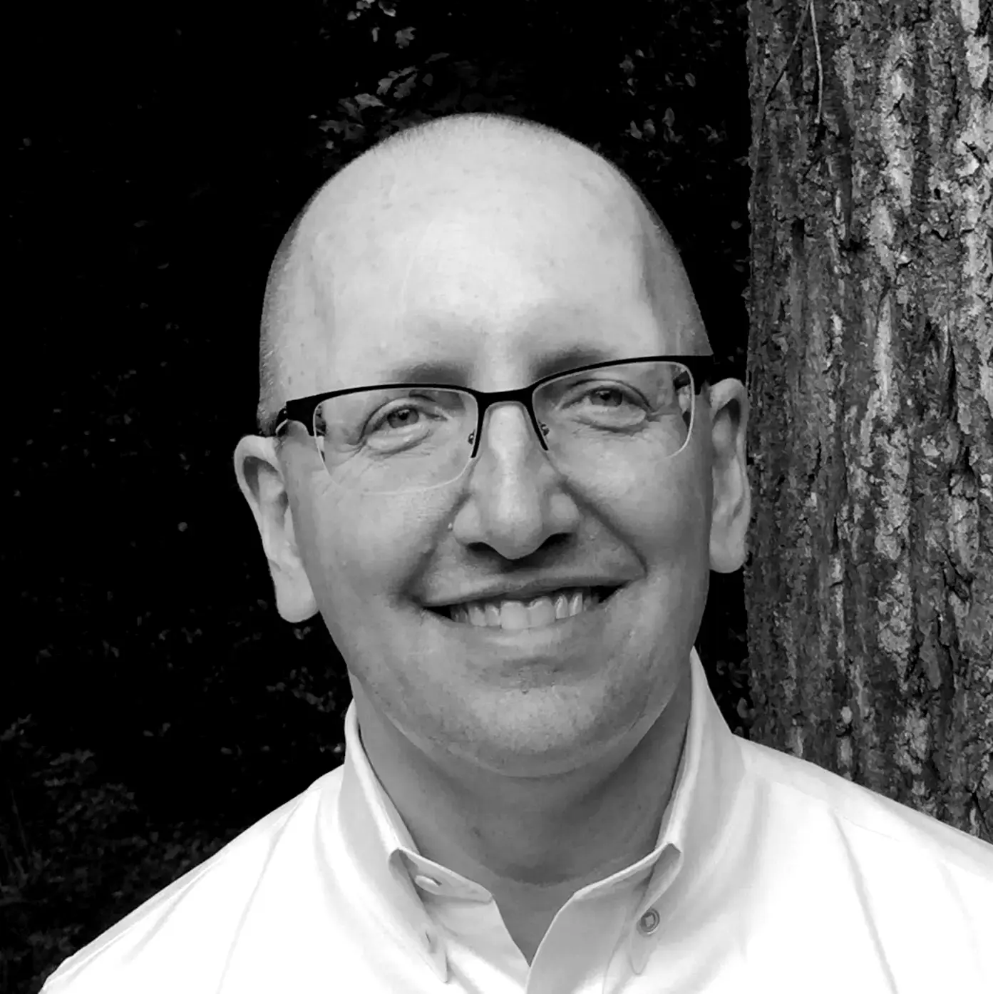 A man with glasses and bald head smiling.